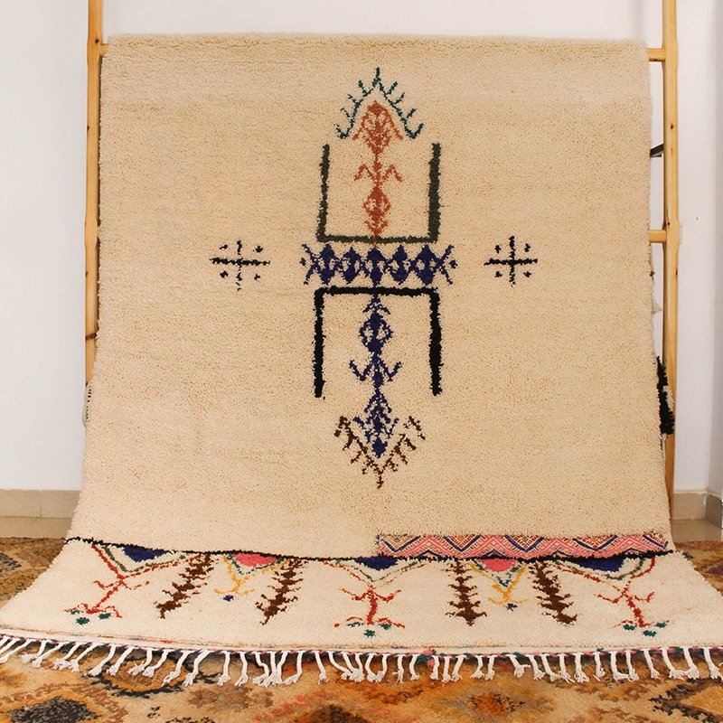 Tapis artisanal écru conçu par Afusart, tissé à la main par Malika, avec motifs amazighs noirs et touches colorées.