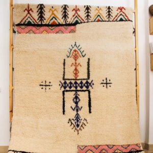 Tapis artisanal écru conçu par Afusart, tissé à la main par Malika, avec motifs amazighs noirs et touches colorées.