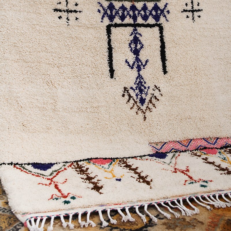 Tapis artisanal écru conçu par Afusart, tissé à la main par Malika, avec motifs amazighs noirs et touches colorées.
