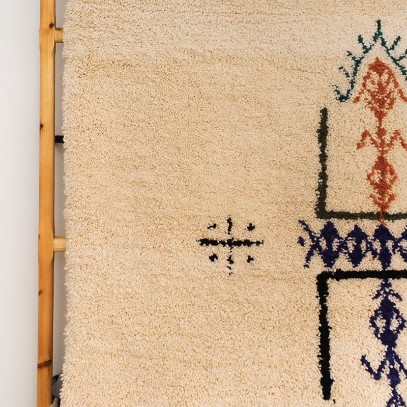 Tapis artisanal écru conçu par Afusart, tissé à la main par Malika, avec motifs amazighs noirs et touches colorées.
