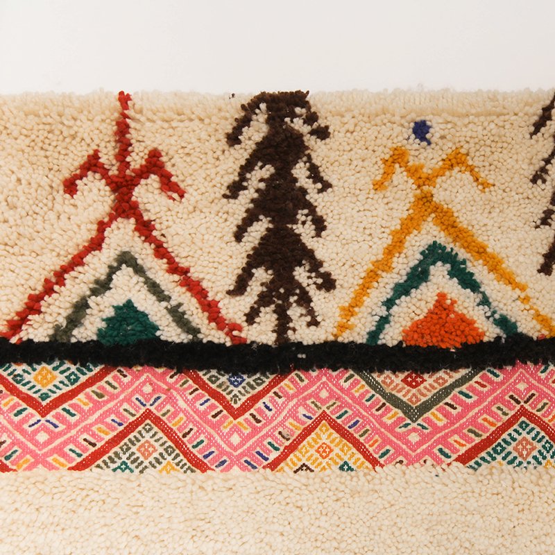 Tapis artisanal écru conçu par Afusart, tissé à la main par Malika, avec motifs amazighs noirs et touches colorées.