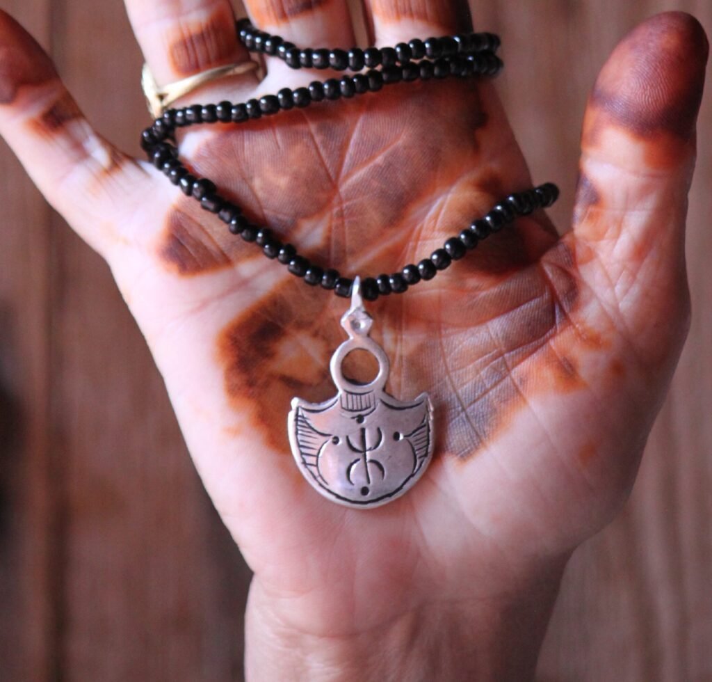 Pendentif amazigh en métal plaqué argent avec motif gravé, monté sur un collier de perles noires.