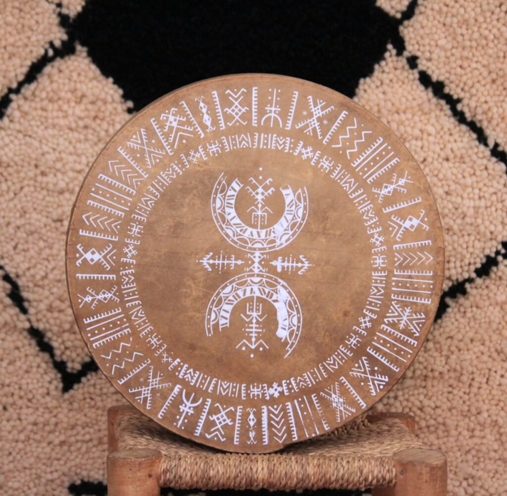 Bendir sérigraphié avec une illustration blanche de Muha Tawargit, composée de motifs géométriques amazighs en cercles concentriques.