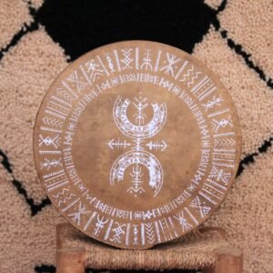Bendir sérigraphié avec une illustration blanche de Muha Tawargit, composée de motifs géométriques amazighs en cercles concentriques.