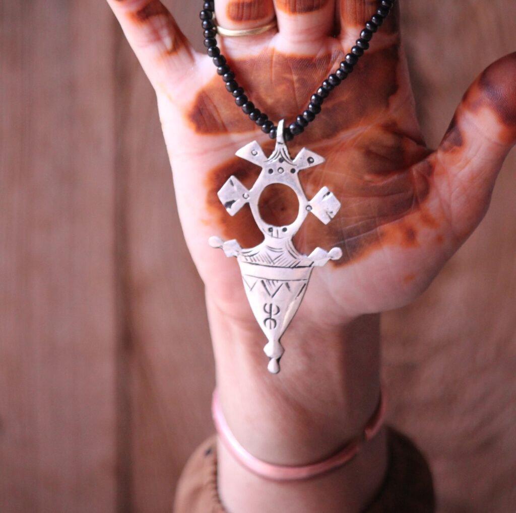 Pendentif amazigh en métal plaqué argent avec motif gravé, monté sur un collier de perles noires.