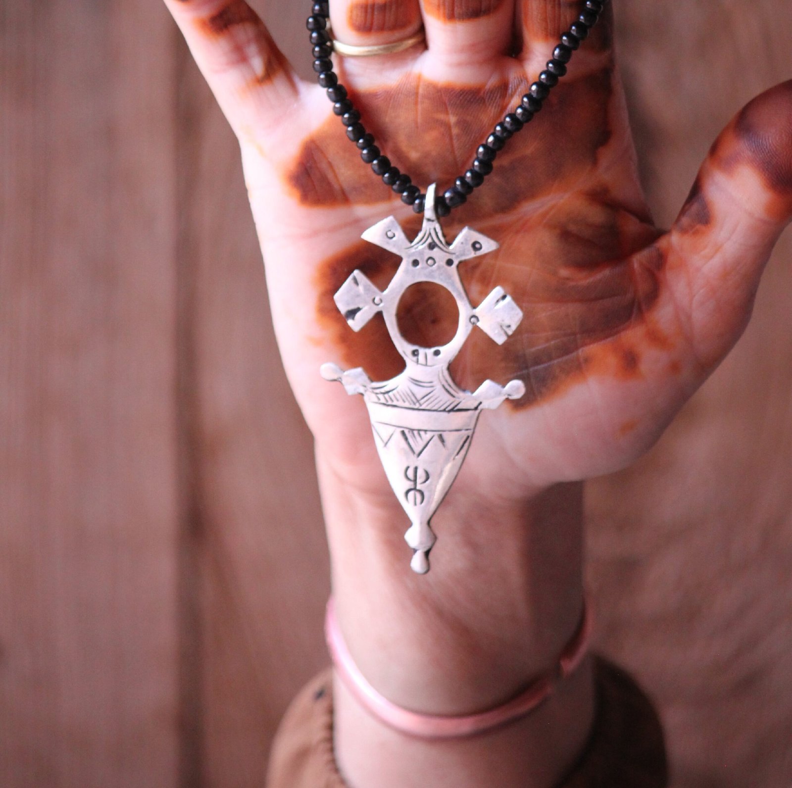 Pendentif amazigh en métal plaqué argent avec motif gravé, monté sur un collier de perles noires.