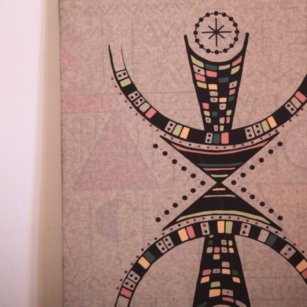 Illustration de Muha Tawargit inspirée du symbole amazigh Aza, composée de formes géométriques noires et de motifs colorés.