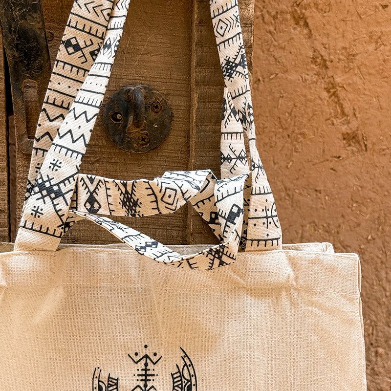 Tote bag beige au design unique Afusart, avec longues et petites anses décorées de motifs amazighs noirs.