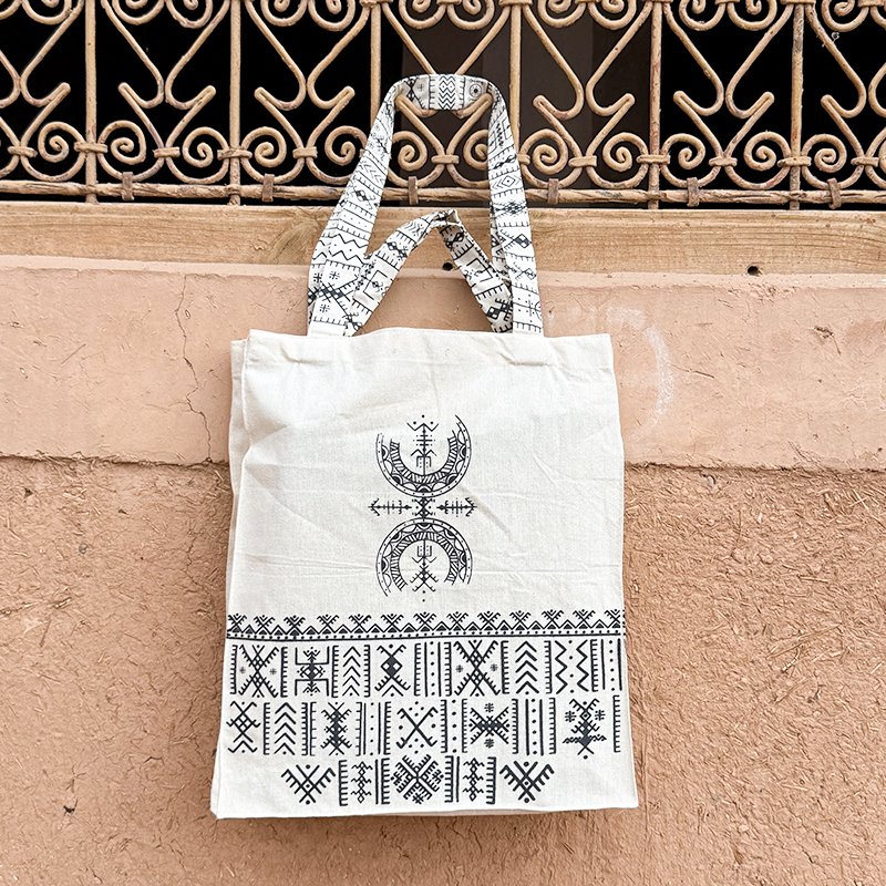 Tote bag beige au design unique Afusart, avec longues et petites anses décorées de motifs amazighs noirs.