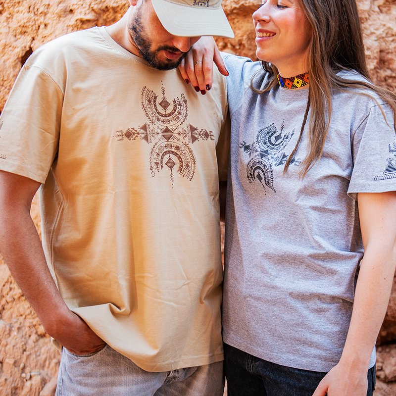 Homme et femme portant des t-shirts Afusart beige et gris, ornés d’un design amazigh inspiré du symbole de liberté Aza.