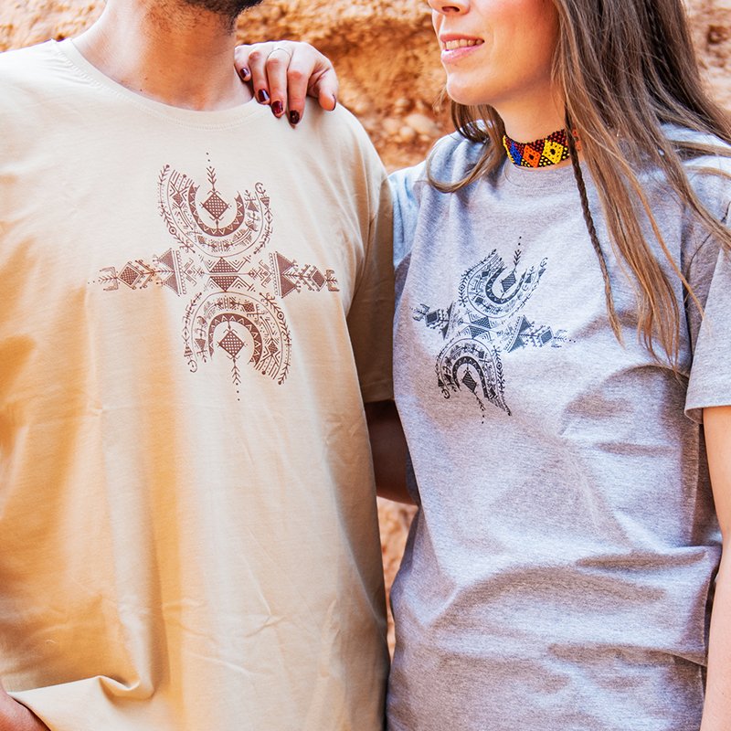 Homme et femme portant des t-shirts Afusart beige et gris, ornés d’un design amazigh inspiré du symbole de liberté Aza.